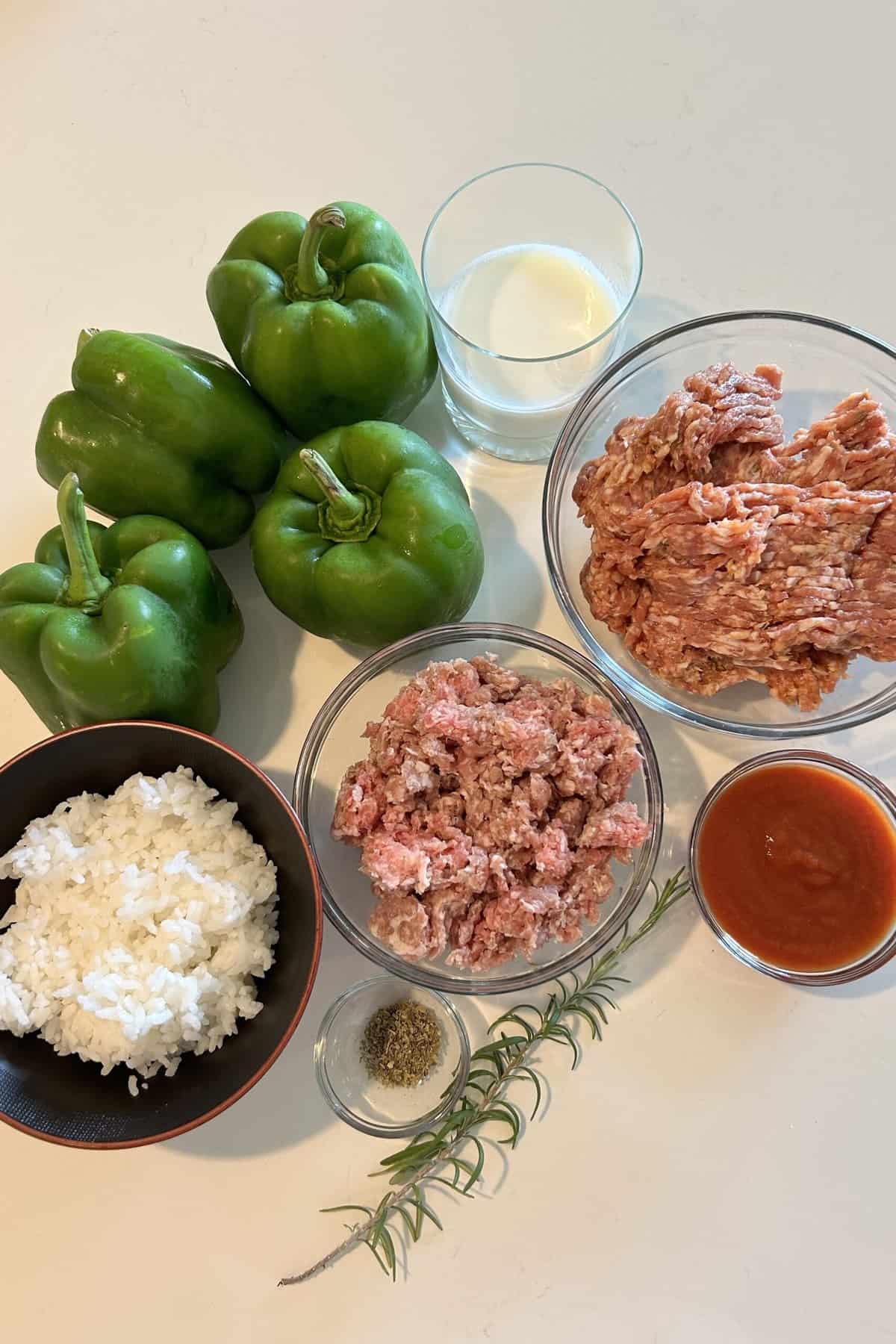 Ingredients for baked stuffed peppers: green peppers, ground pork, Italian sausage, white cooked rice, milk, egg, Italian seasonings, fresh rosemary, tomato paste