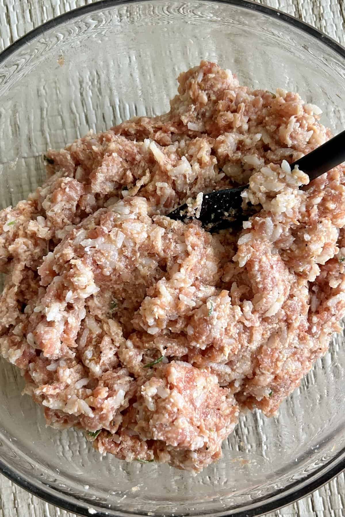 Mixture of ground pork, Italian sausage, cooked rice and ingredients in a glass bowl