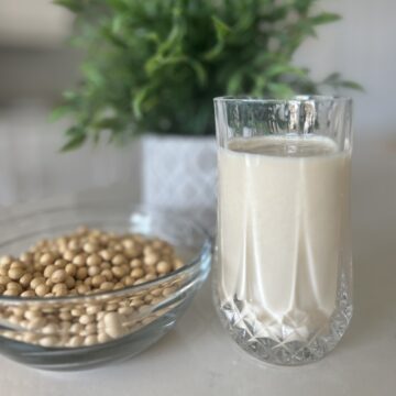 A bowl of dry soybeans and a glass of rich silky smooth soy milk