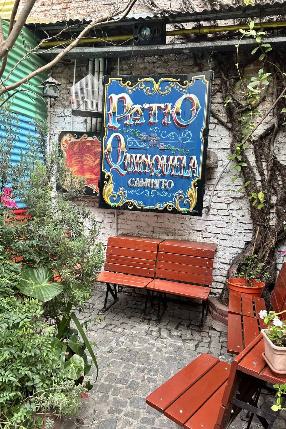 Red benches, plants, flowers and a blue sign with words Patio Quinquela Caminito in a nook for resting and taking pictures