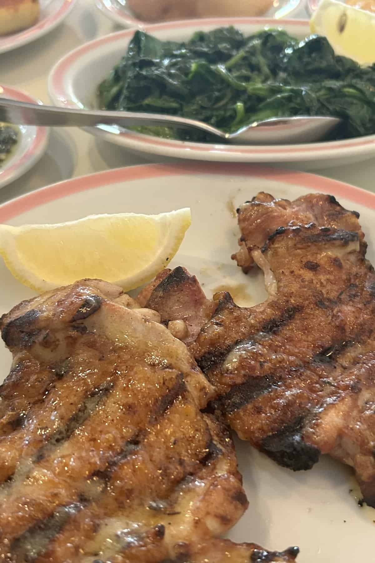 Two pieces of juicy roasted chicken thigh (pasta y muslo al homo a carbon) and a lemon wedge on a plate. Served at El Preferido de Palermo.