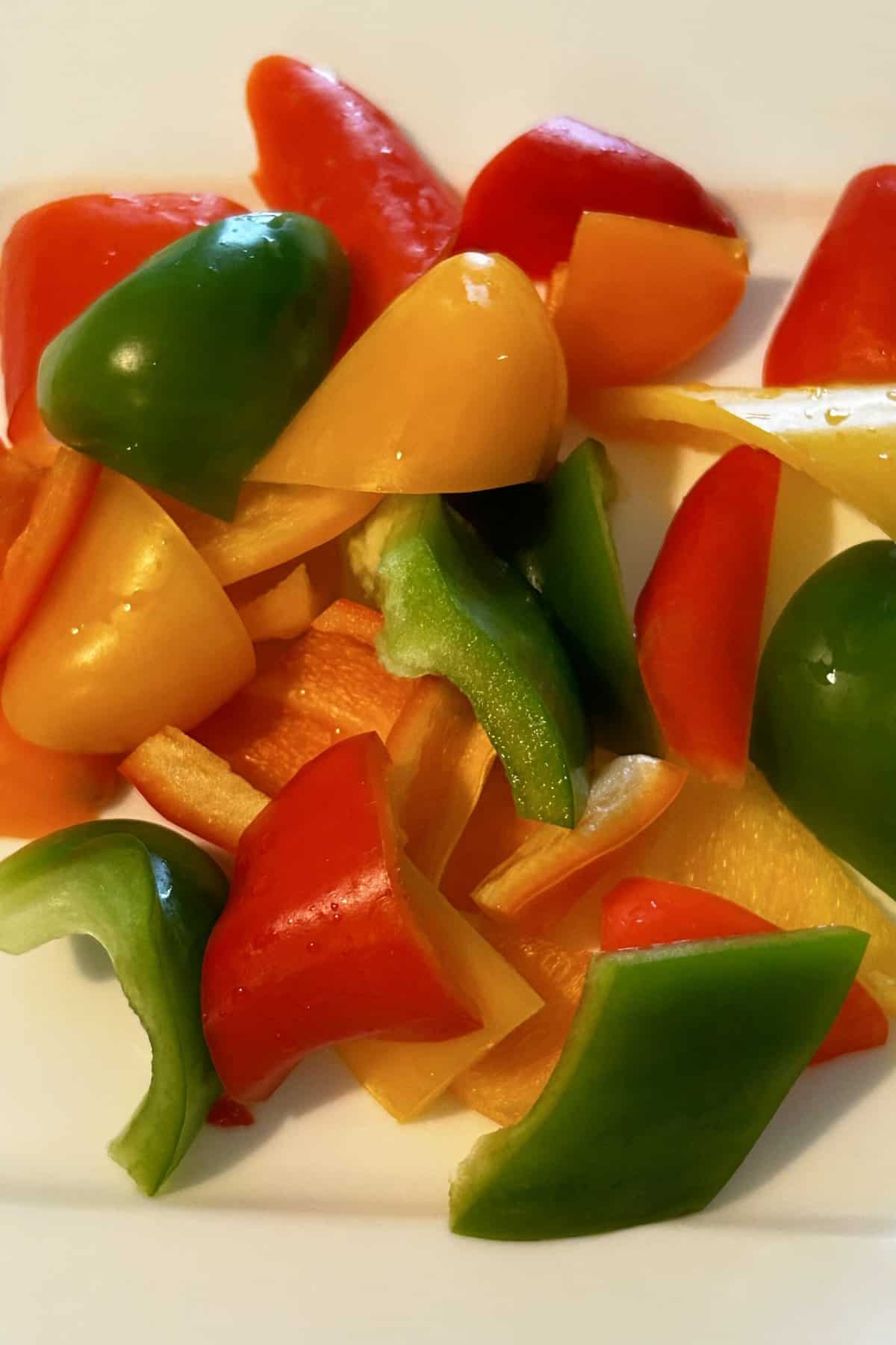 Green, red, yellow, orange peppers cut up on a white plate