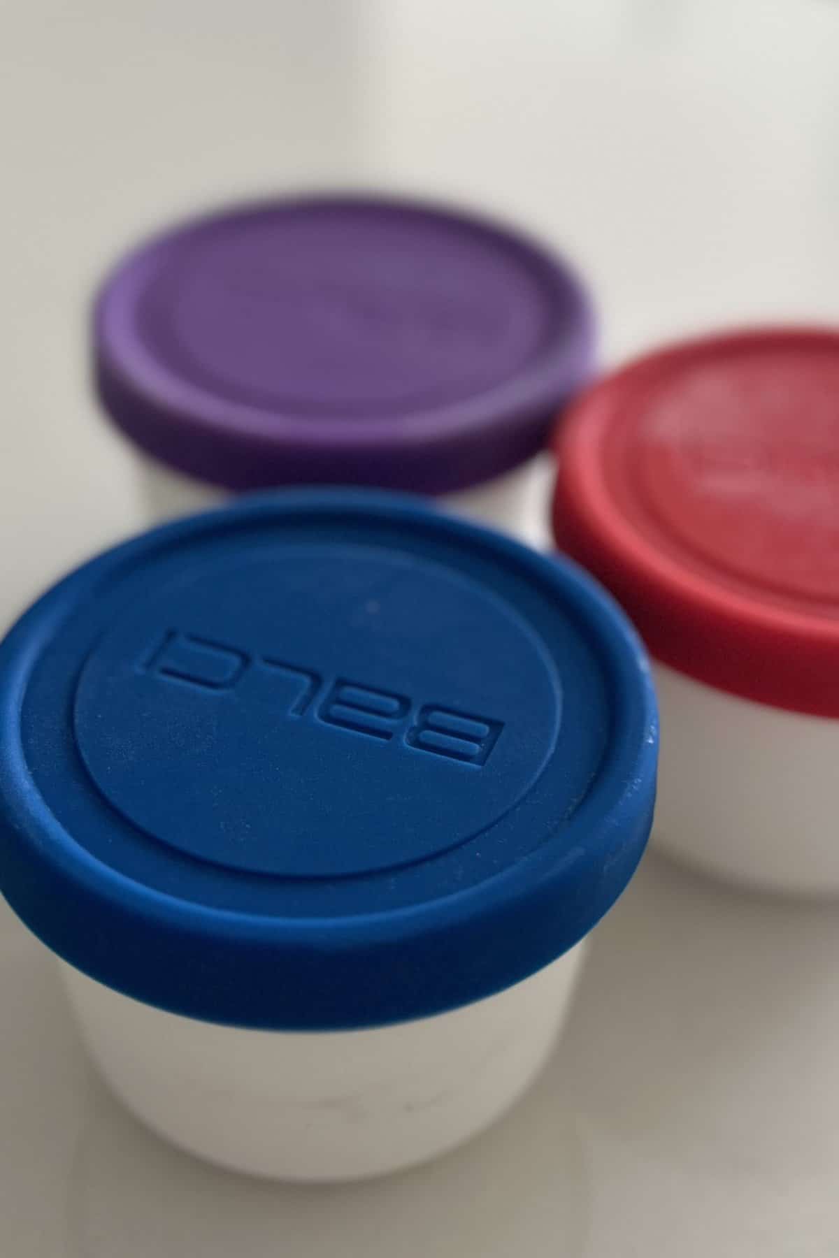 Mini ice cream containers covered with lid ready to be put in the freezer. The lid colors are blue, red and purple.