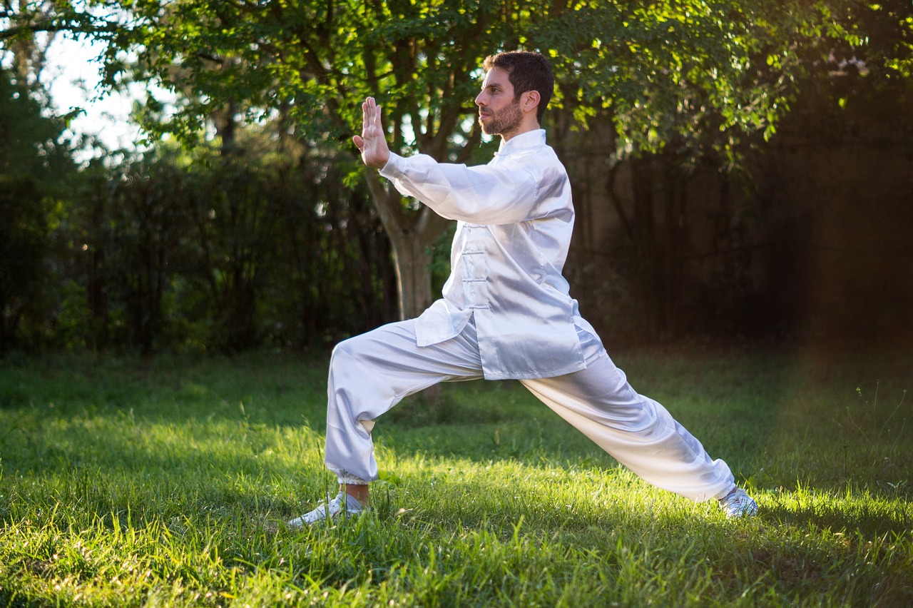 A guy wearing white Chinese clothes doing Tai Chi in a park