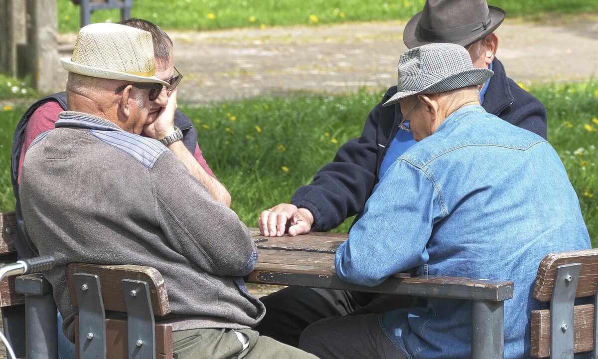 Four old gentlemen sitting and playing game outdoor. Three of them wear hats.