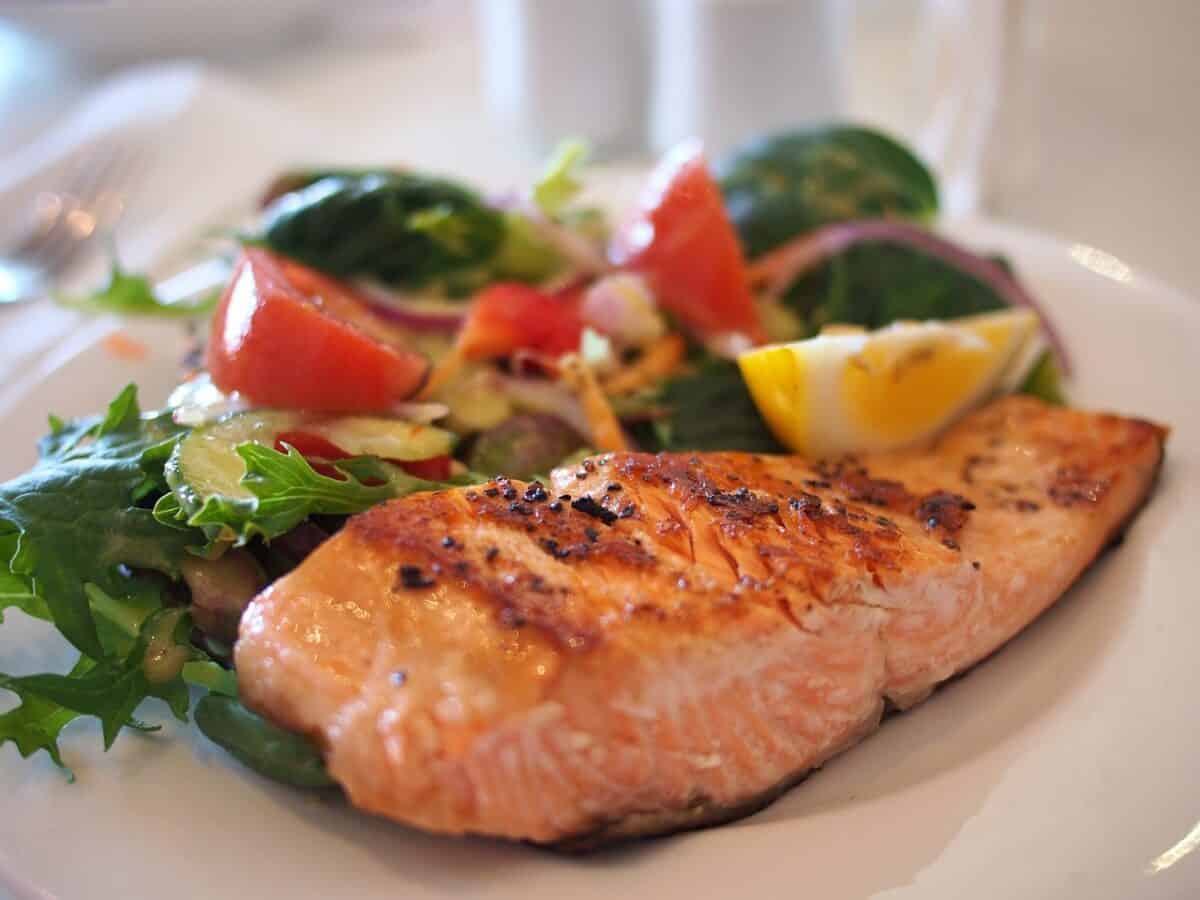 Grilled salmon, salad greens, cherry tomatoes and a slice of lemon on a white plate