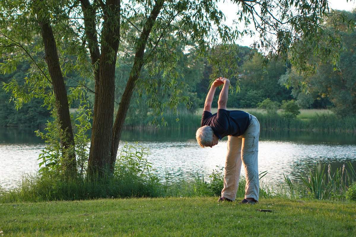 A senior in is bending forward with legs straight and hands together pointing toward the sky.