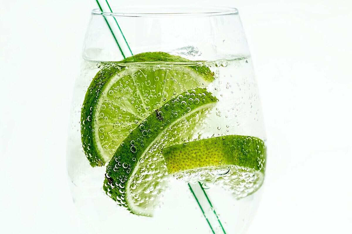 Refreshing cold lime drink with three half slices in a clear glass tumbler and a straw