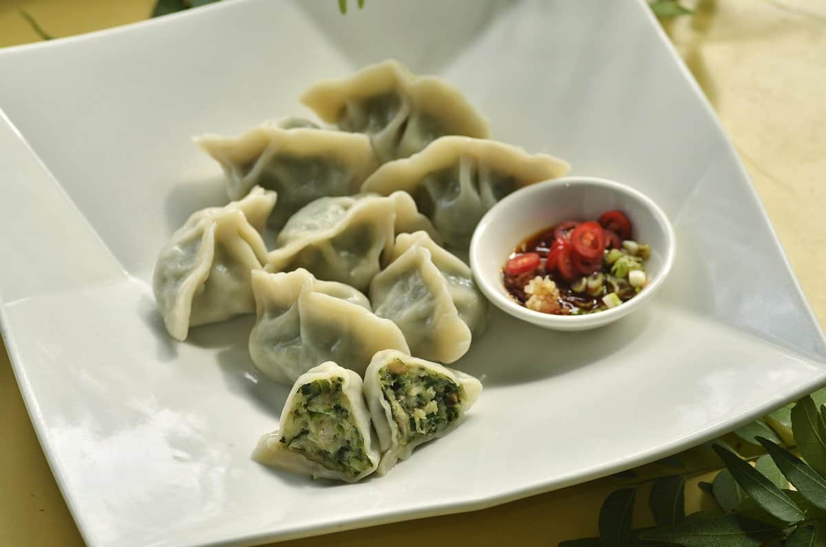 Chive dumplings in a white plate with dipping sauce